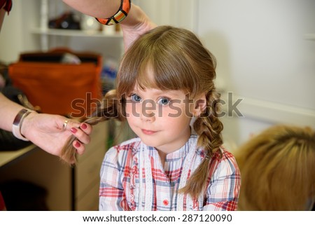 Preparation for children\'s photo shoot. Hairdresser makes hairstyle of two braids girl