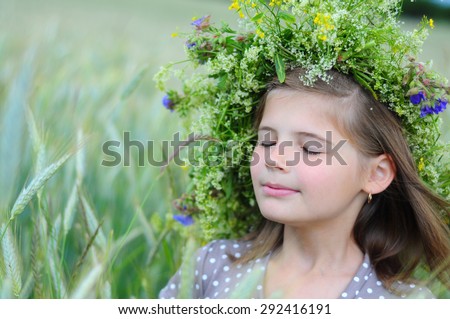 Smiling girl with closed eyes in the field in the ears. Floral wreath on head