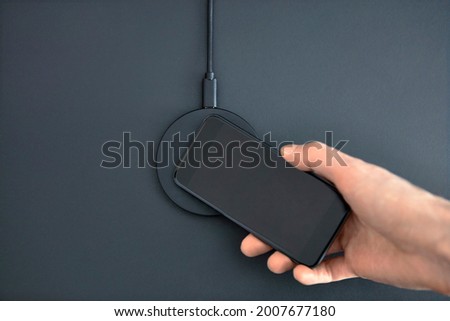 Male hand putting smartphone on wireless charger to recharge battery. Round device laying on office desk. Modern technology, wireless device and transfer of energy concept. Foto stock © 