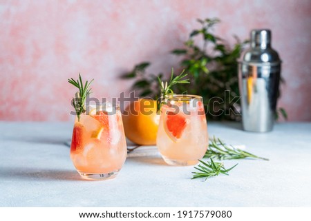Tequila cocktail or cold lemonade with grapefruit juice, tinted with the aroma of a fresh sprig of rosemary on fashion pastel pink background.