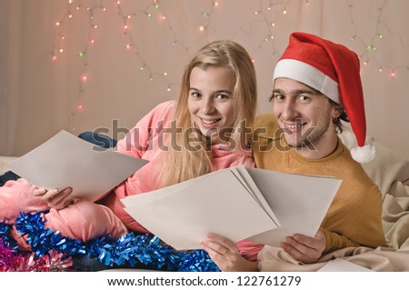 young happy couple on bad in new year decorations with sheets of photos, garland is behind them