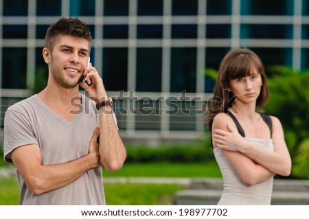 Portrait of a young man using a mobile phone and sad woman. focus on man