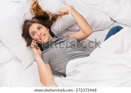 Above view of young brunette in casual clothes lying on bed and speaking on the phone