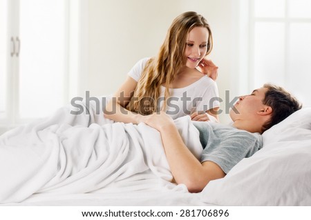 Sexy young couple kissing and playing in bed on light window background