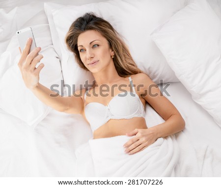 sexy young woman lying on the bed and make a selfie. Above view
