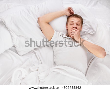 Young handsome happy man waking up on bed, top view