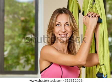 Young woman posing and holding anti-gravity aerial yoga green hammock indoor