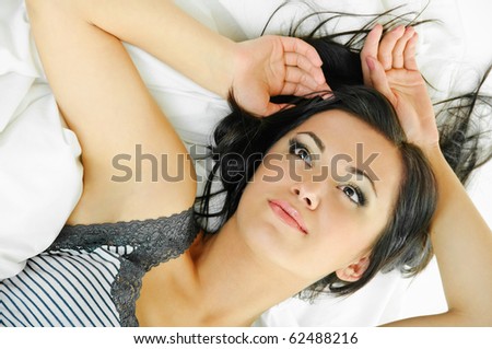 portrait of smiling beauty brunette on white bed clothes
