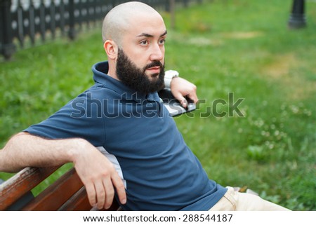 Bearded bald man sitting on a bench with tablet at the alley
