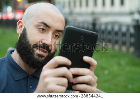 Bearded bald man sitting on a bench and game on tablet at the alley