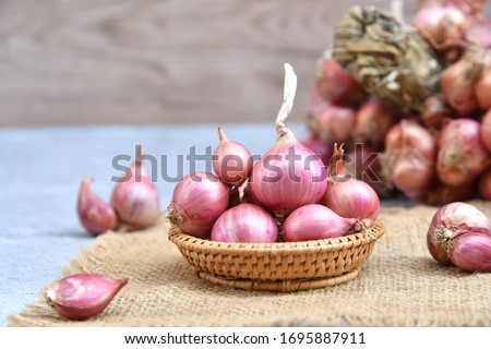 Thai red onion or Shallots. Fresh purple shallots on bamboo basket with old wallpaper and shallots bunch background. Selected focus. Concept of spices in healthy cooking Foto d'archivio © 