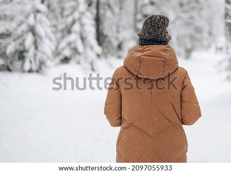Photo of Half length portrait of brunette girl wearing brown long jacket and hat. standing pose in snow forest