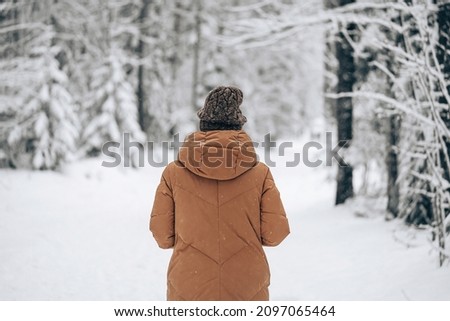 Photo of Woman in winter warm jacket walking in snowy winter pine forest. View from back.