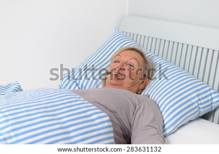 Sick Middle Aged Woman Lying Down on Bed with Thermometer in Mouth While Looking up in Pensive Facial Expression.
