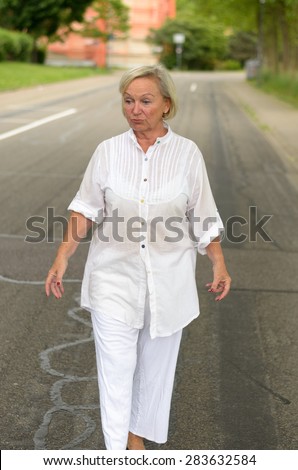 Portrait of a Middle Aged Blond Woman in All White Outfit, Walking at the Street Alone in Serious Facial Expression.