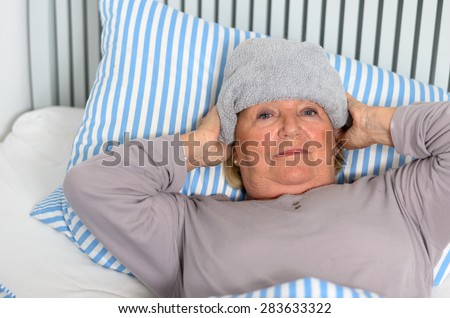Sick Middle Aged Woman Lying Down on Bed with Towel on the Forehead While Looking up in Pensive Facial Expression.