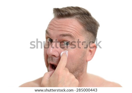 Middle-aged man applying moisturizer to his skin to ward off the signs of ageing in a skincare and pampering concept, head shot on white
