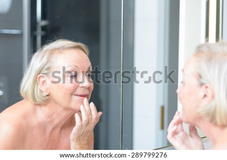Senior lady checking her skin in the mirror leaning forwards for a closer look as she hold a finger to her forehead