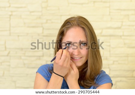 Pretty young woman applying eyeliner to her eye to enhance and outline the eye in a fashion and beauty concept