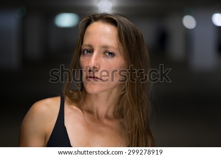 Serious woman wearing a summer top standing looking speculatively at the camera with a sideways glance in a shadowy environment