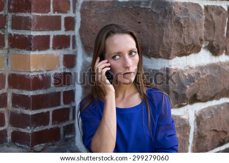 Serious woman standing at the corner of a building listening to a call on her mobile phone and staring thoughtfully to the side with a serious expression, head and shoulders
