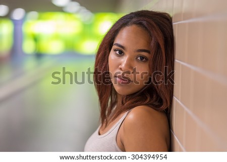 Close up Pretty African-American Young Woman Leaning Against Wall Inside a Building and Smiling at the Camera.