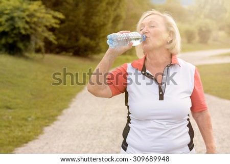 Healthy senior woman drinking bottled water as she takes a break while out jogging on a rural road in a health and fitness concept