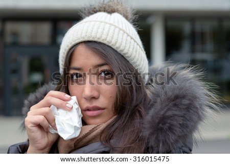 Sad tearful woman in warm winter fashion holding a handkerchief to her face to dry the tears from her eyes looking into the camera