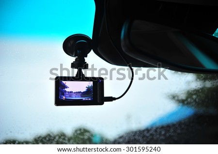 Car video recorder next to a rear view mirror in highway sunset.