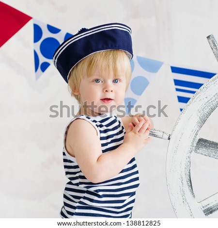 Portrait of a cute little boy in the striped vest and sailor hat holding wooden steer wheel