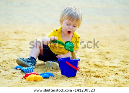 Concentrated toddler playing with his toy bucket and shovel in the sandpit