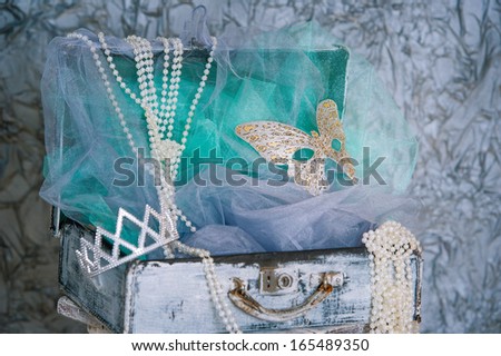 Closeup vintage style suitcase with pearl beads, crown and mask