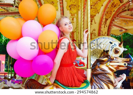 Lifestyle concept, happy young woman with colorful latex balloons in the amusement park riding a carousel