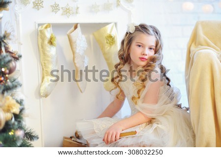 Christmas time, adorable girl with lovely curls sitting by the fireplace with stockings