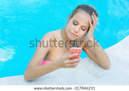Trendy young woman texting in the swimming pool using her cell phone
