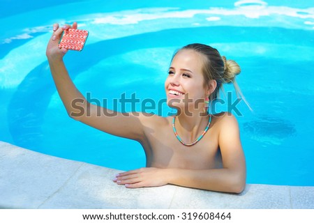 Pretty young blonde woman taking selfie picture with her phone in the swimming pool