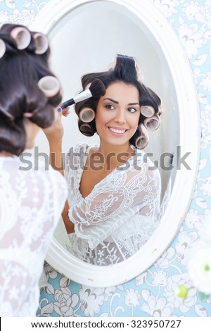 Beautiful woman in hair curlers puts on morning makeup with powder brush