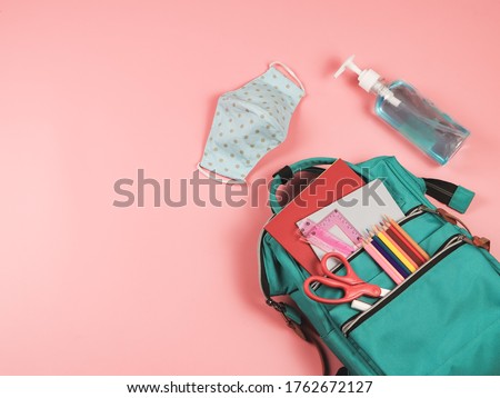 COVID-19 prevention while going back  to school  and new normal  concept.Top view of backpack with school supplies , blue polka dot fabric masks and sanitizer gel on pink background.