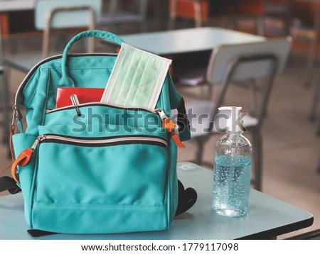 COVID-19 prevention , back  to school  and new normal  concept.Front view of  backpack with school supplies ,surgical mask and sanitizer gel on school desk in classroom.