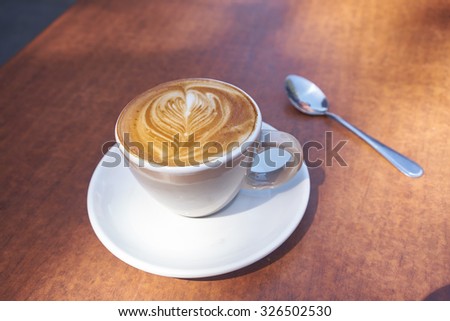 coffee in white mug and plate with coffee art on wooden table