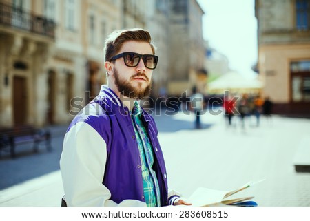 Stylish young bearded guy with map looking to the side on the streets of old European city
