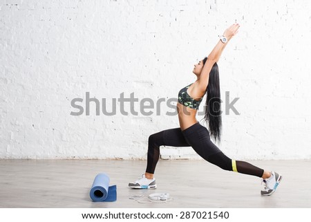 Sporty yogi brunette girl doing exercises, asana Anjaneyasana, low lunge yoga pose. In sports outfits with beautiful body, against concrete wall.