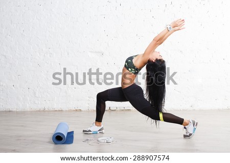 Sporty yogi brunette woman doing exercises, asana Anjaneyasana, low lunge yoga pose. In sports outfits with beautiful body, against concrete wall.