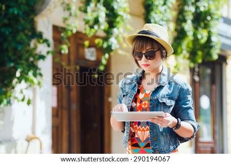 Young pretty woman tourist using tablet travel app guidebook ebook on in the old European city. Hipster style glasses and hat.