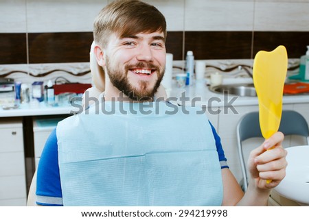 Happy young man with mirror smiling in the dentists chair.
