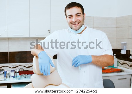 Portrait of a smiling dentist leaning against dentists chair in dental clinic