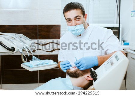 Dentist in medical mask examining man teeth in the dentists chair.