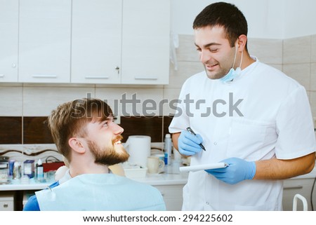 Male dentist and taking notes, with happy patient, at the dental office.