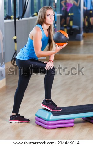 Full length of pretty brunet young woman with ball is performing step aerobics exercise in gym