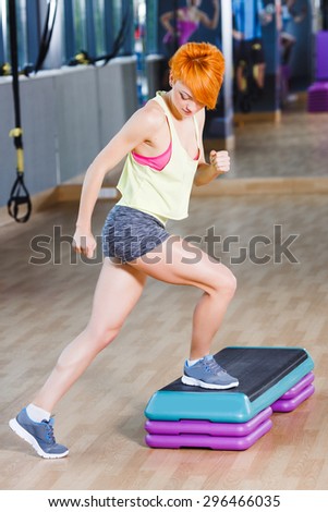 Athletic redhead young woman performing step aerobics exercise in gym
